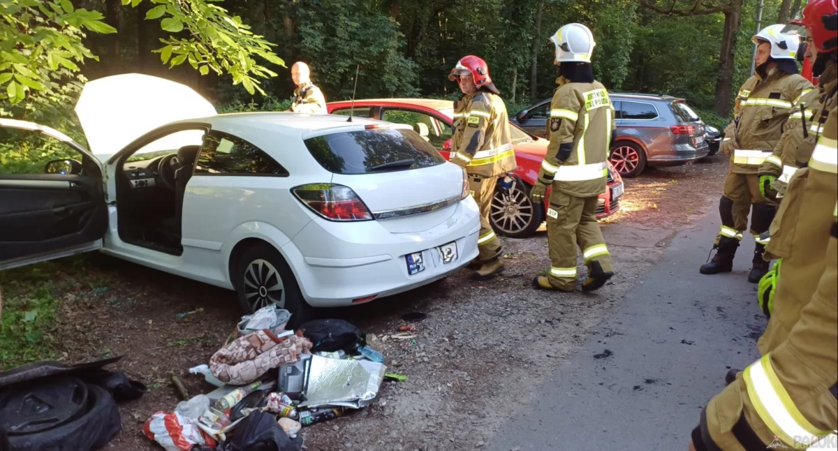 Strażacy zmuszeni zostali do mechanicznego otwarcia bagażnika. W tym celu wybili przednią, lewą szybę od strony kierowcy. Otworzyli też maskę pojazdu w celu odłączenia akumulatora i instalacji gazowej. Z bagażnika wyjęli wszystkie znajdujące się tam przedmioty, w tym rzeczy osobiste, koc, ubrania i nadpalony pokrowiec z kołem zapasowym. Przy bagażniku samochodu na ziemi leżały niedojedzone kawałki grillowanej kiełbasy. fot. Magdalena Lachowicz